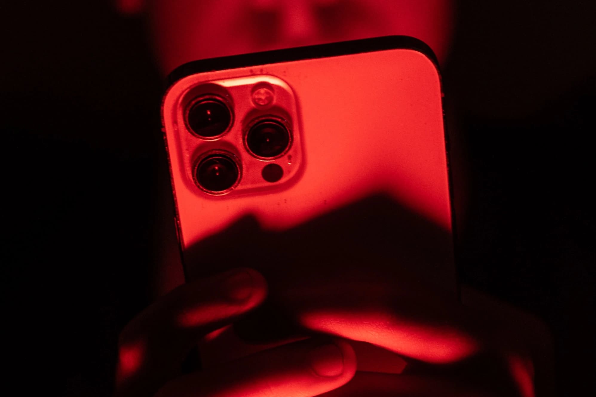 Pessoa segurando um iPhone diante de um fundo vermelho