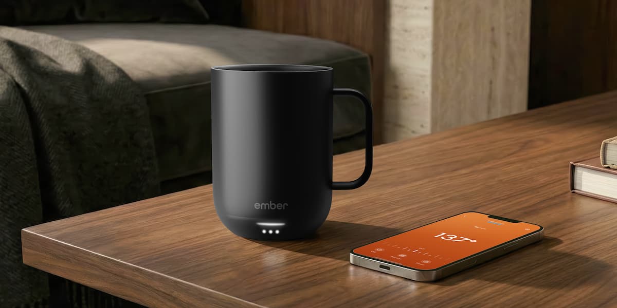 Caneca inteligente Ember Mug 3 preta sobre uma mesa ao lado de um celular